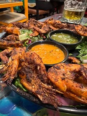 Grilled shrimp plate with spicy sauce and beer in restaurant setting
