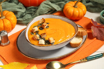 Bowl of delicious pumpkin cream soup with seeds, croutons and autumn leaves on white wooden background