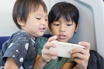 電車内でスマートフォンを閲覧している子供達　アジアの日本人の兄弟