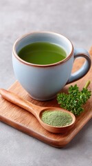 Top Down Food Photo Of A Cup Of Green Tea And Spoon With Matcha Powder And Fresh Parsley Garnish On A Wooden Board And Textured Gray Background