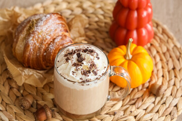 Cup of pumpkin latte with croissant and autumn decor on table in living room, closeup