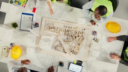 Time lapse top down view zoom out of real estate developers and architects in office reviewing blueprints and 3D models. Development team discusses urban planning and property investment. Camera A.