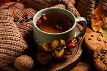Composition with mug of rose hip tea, cookies and sweater on wooden background, closeup