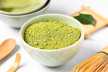 Bowl of fresh matcha tea with powder, chasen, chashaku and spoon on white background