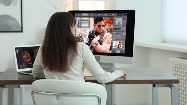 Professional retoucher editing photo on computer and laptop at table in office, back view