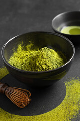 Bowl with powdered matcha tea and chasen on black grunge background