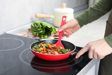 Woman stirring mix of fresh vegetables with slotted spatula in frying pan, closeup
