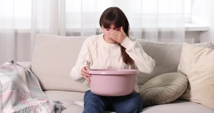 Young woman with basin suffering from stomachache and nausea at home