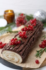 Delicious Yule log (traditional Christmas cake) with redcurrant on white table, closeup
