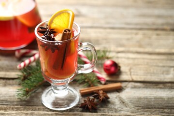 Tasty punch drink in glass, spices and Christmas decor on wooden table, closeup. Space for text