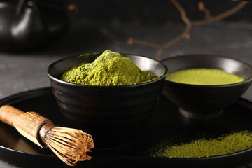 Bowl of fresh matcha tea with powder and chasen on black grunge background