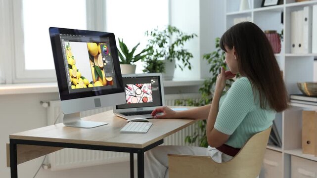 Professional retoucher editing photo on computer and laptop at table in office