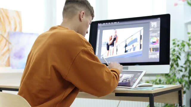 Professional retoucher editing photo on computer and tablet at table in office