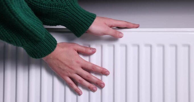 Woman warming her hands near radiator indoors, closeup