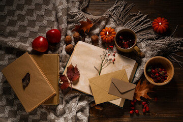 Books with cup of tea, fruits, envelopes, scarf and autumn decorations on brown wooden background