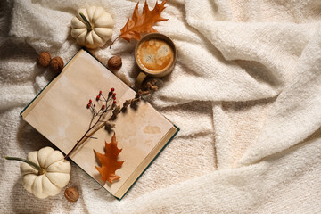 Book with cup of coffee, pumpkins and autumn decorations on warm white plaid background