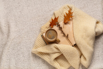 Book with cup of coffee, sweater and autumn decorations on warm white plaid background