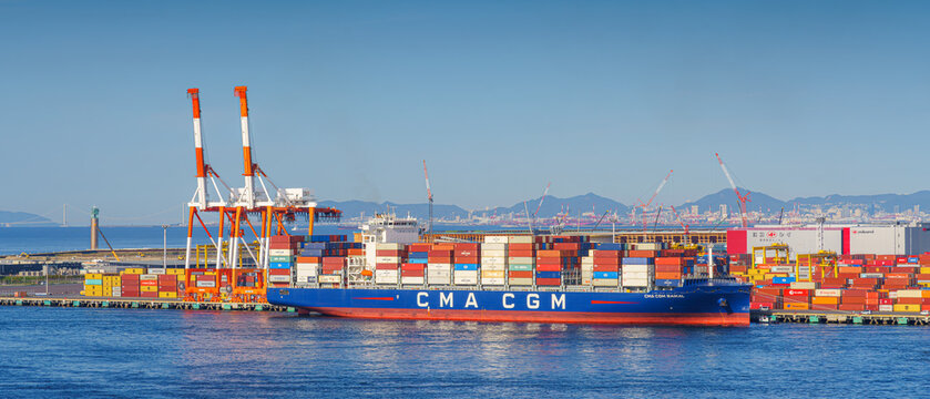 Osaka, Japan - Oct 11 2024, panoramic sea view of the docks of the Osaka Commercial Port with a heavily loaded CMA CGM cargo ship moored during the daytime, Osaka, Japan