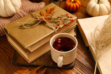 Books with cup of tea, sweater and autumn decorations on brown wooden background