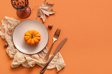 Beautiful table setting with pumpkin, acorns and autumn leaf on orange background