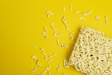 Flat lay of raw instant noodles with scattered crumbs on bright yellow background, minimal style with copy space, modern food concept for design or advertising.