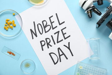 Composition with microscope, petri dishes and NOBEL PRIZE DAY greeting card on blue background....