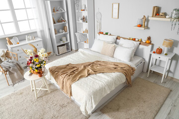 Comfortable bed, table and pumpkin with autumn bouquet in interior of bedroom