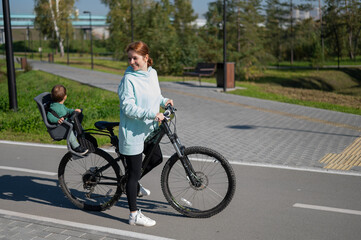 Obraz premium Caucasian woman rides bicycle with one-year-old son in park. 
