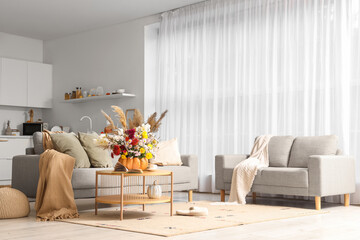 Interior of living room with comfortable sofas, table and pumpkin with autumn bouquet