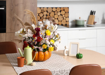 Pumpkin with autumn bouquet, teapot and cup on table in kitchen, closeup