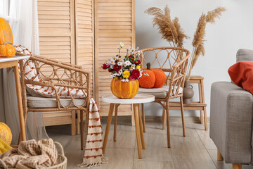 Wicker chairs, table and pumpkin with beautiful autumn flowers in interior of living room