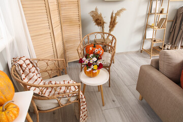 Wicker chairs, table and pumpkin with beautiful autumn flowers in interior of living room
