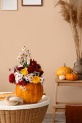 Pumpkin with beautiful autumn flowers on table in interior of living room, closeup