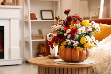 Pumpkin with beautiful autumn flowers and cup of tea on table in living room, closeup