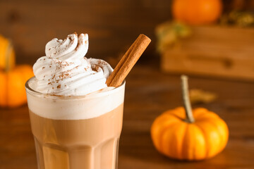 Glass of hot pumpkin latte with whipped cream and cinnamon on wooden background, closeup