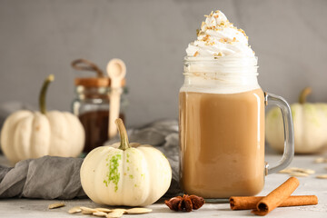 Mason jar of hot pumpkin latte with whipped cream and cinnamon on grey background
