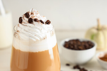 Glass of hot pumpkin latte with whipped cream and coffee beans on white background, closeup