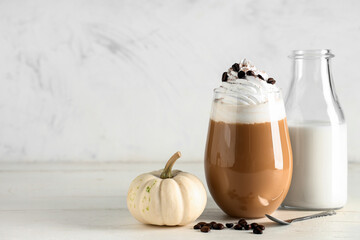 Glass of hot pumpkin latte with whipped cream and coffee beans on white wooden table