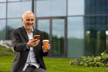 Mature businessman smiling using smartphone drinking coffee on break