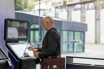 Mature businessman interacting with modern self-service digital kiosk system