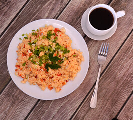 Egg omelette with tomatoes and chopped parsley on a wooden table, a cup of black coffee and a fork nearby.