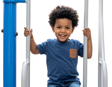 Happy young boy with curly hair smiles, holding metal bars of playground equipment, wearing a blue shirt