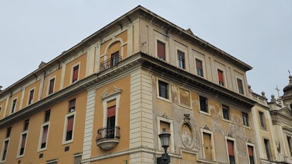 Rome, Italy - 11 January 2025. Corner of Tempio dei Giovani-Panzieri Fatucci with faded facade, closed red shutters, sculpted window frames, and an upper balcony under overcast daylight.