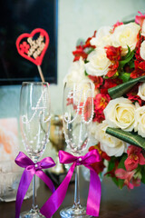 Two elegant champagne glasses decorated with pearls and purple bows on a soft pink tablecloth. Symbol of celebration, love, and joyful wedding reception