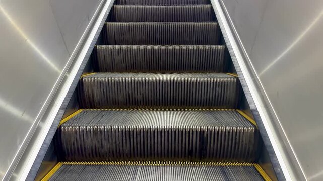 A straight-on, low-angle view, moving escalator ascending upwards, human shadow on the way walking up the escalator, emphasizing the repeating pattern steps sharp, reflective lines of the stainless st