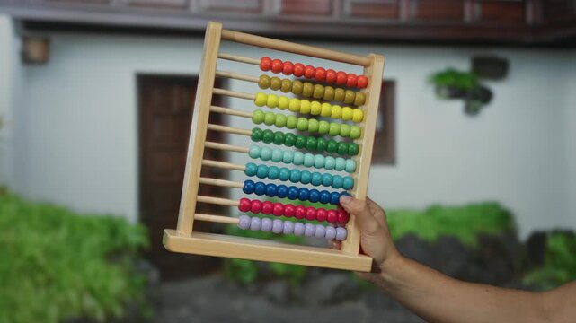 Man holding colorful abacus outside on a city street with a house in the background, showcasing vibrant beads against a suburban town setting.