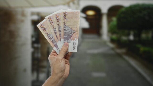 Man holding icelandic krona banknotes on a city street illustrating financial concept with caucasian hand showing currency outdoors during daytime in urban setting.