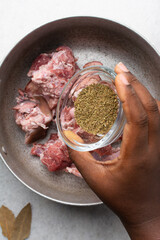 Overhead view of seasoned raw goat meat in a pot, top view of chopped goat meat being prepared for cooking