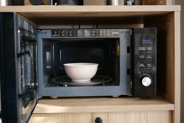 Fototapeta premium Microwave with a bowl inside on a kitchen shelf