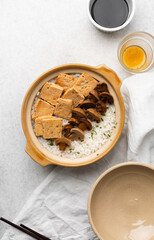 Overhead view vegan claypot rice with pan fried tofu, mushrooms and scallions, top view of crispy rice in a donabe on a marble countertop